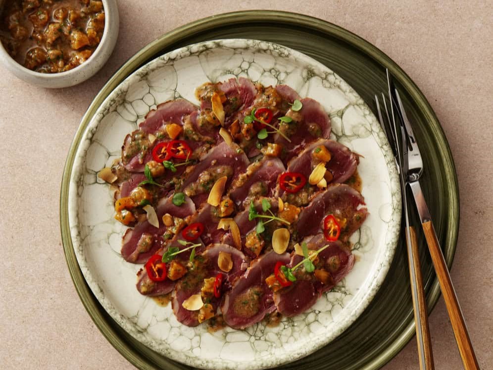 Carpaccio van gerookte eend met amandeldressing op een bord met bestek ernaast