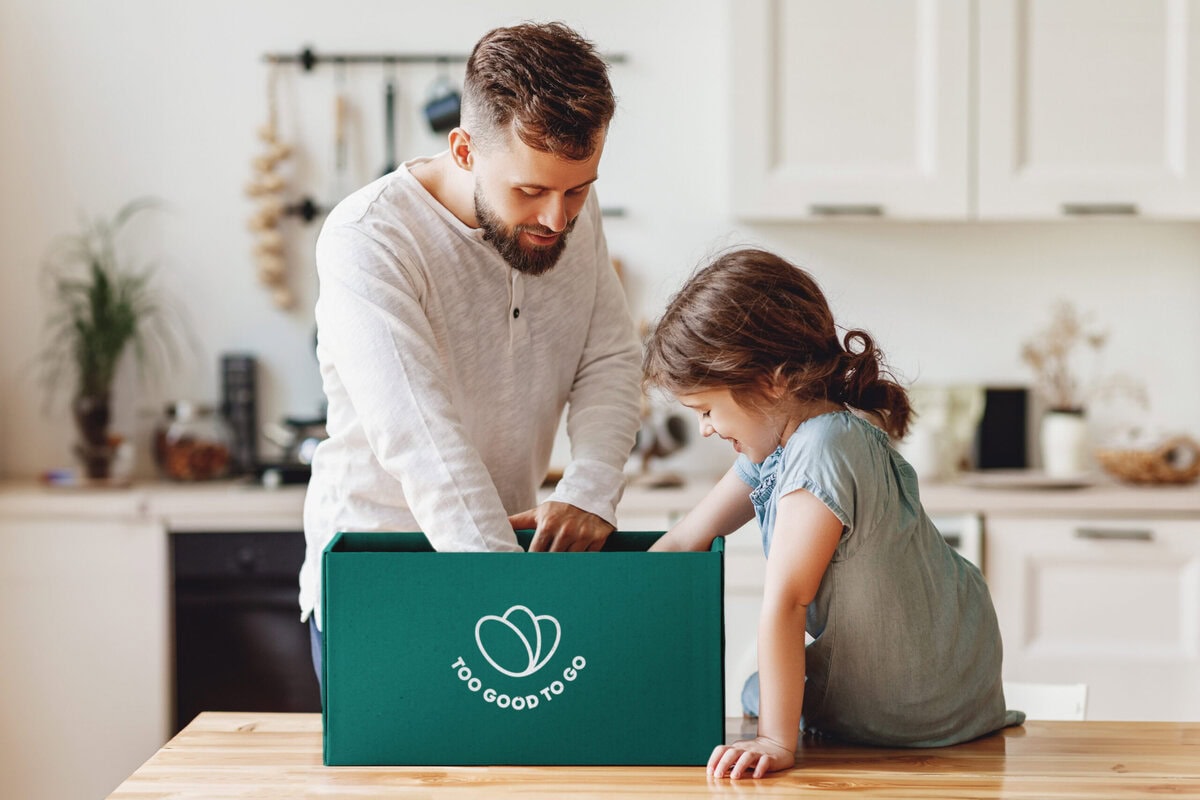 Man met kind bij een pakket van Too Good To Go voor tijdens een autovakantie