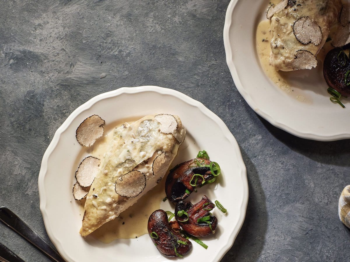 Gestoofde kip met truffel-roomsaus met plakjes truffel erop en champignons ernaast