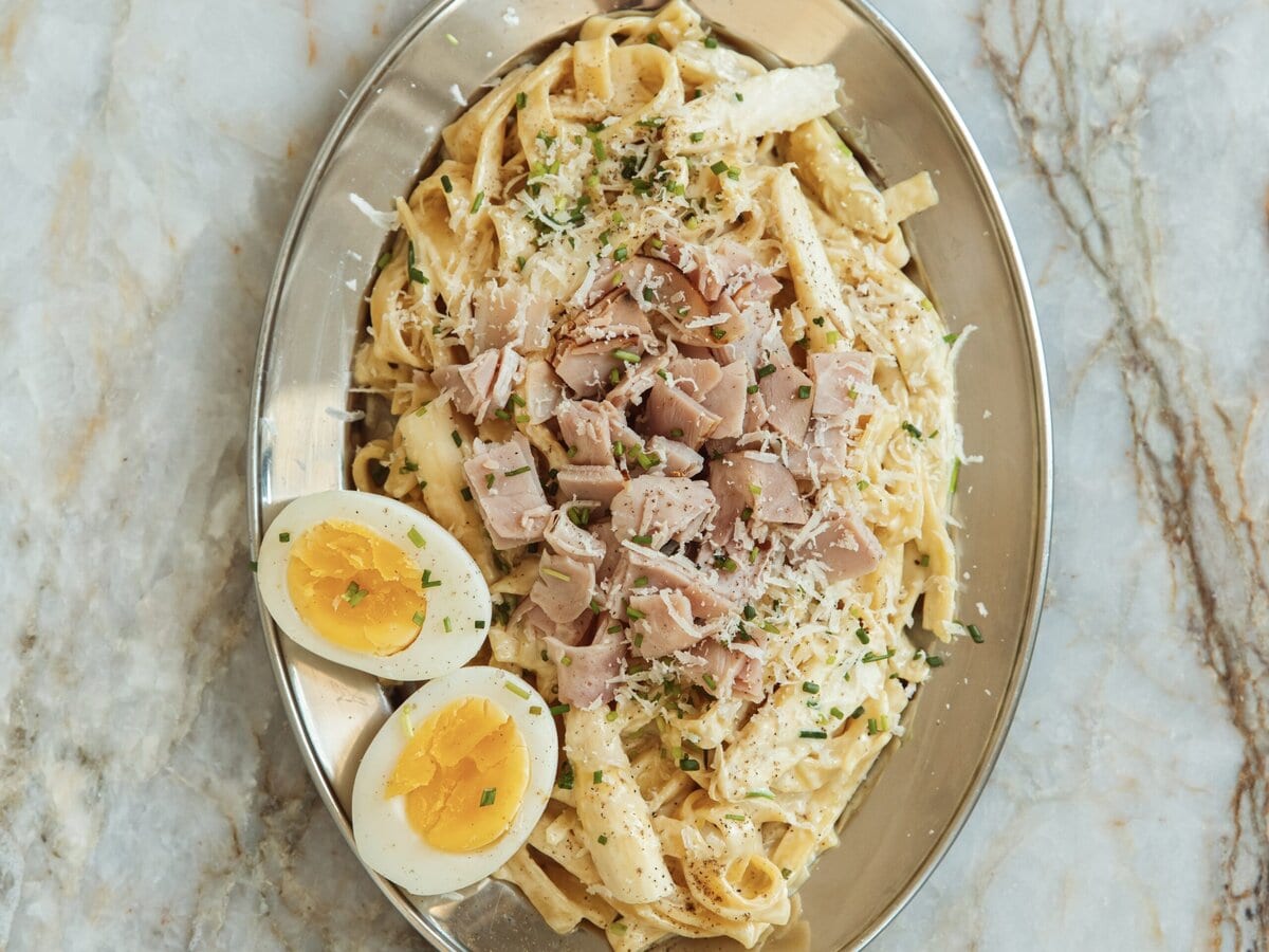 Tagliatelle in een saus van asperge met stukjes ham, parmezaanse kaas en bieslook erover, met ernaast een eitje