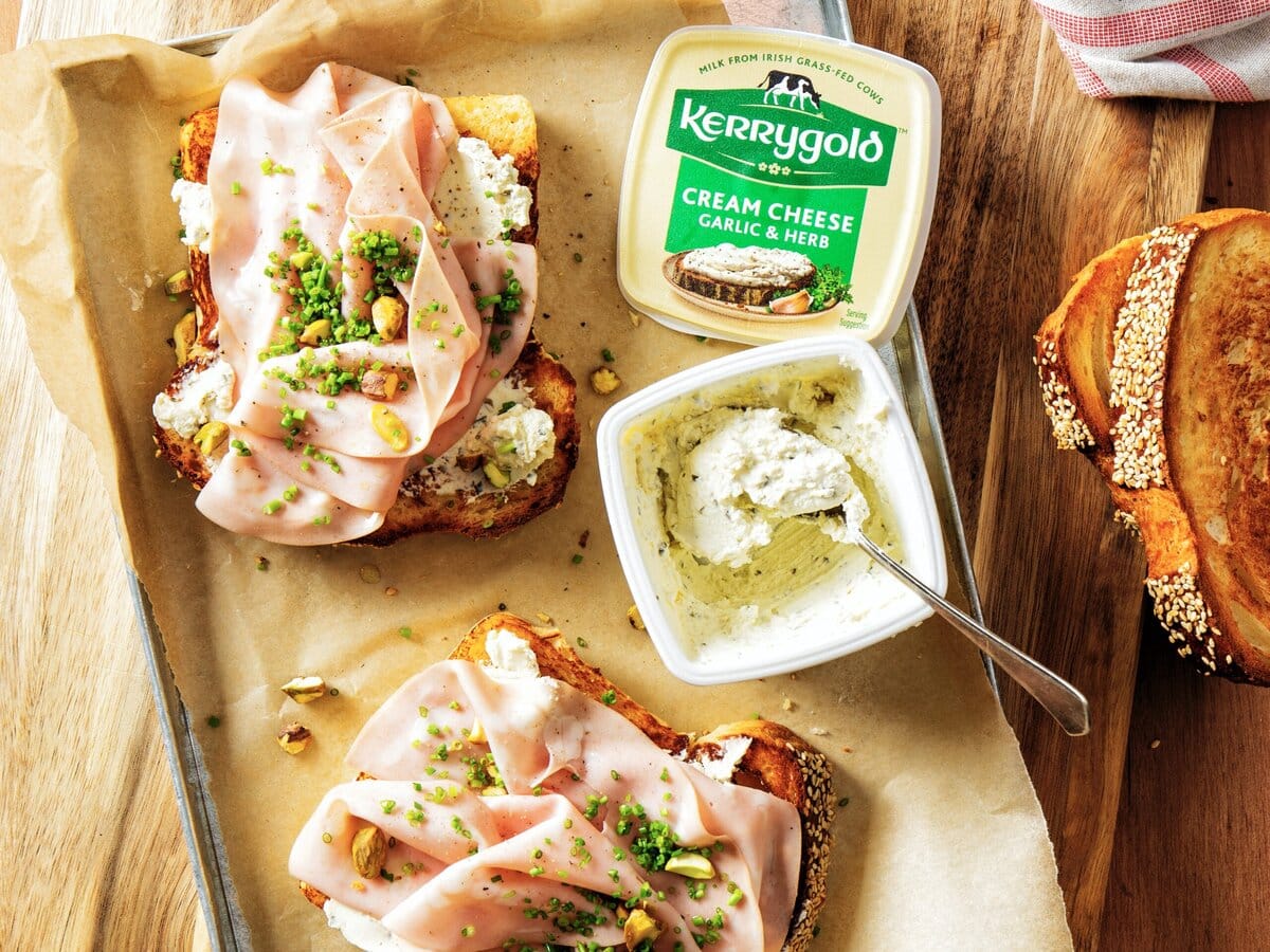 Twee briochetoasts met kruiden creamcheese, mortadella, pistachenootjes en bieslook met een bakje Kerrygold boter ernaast