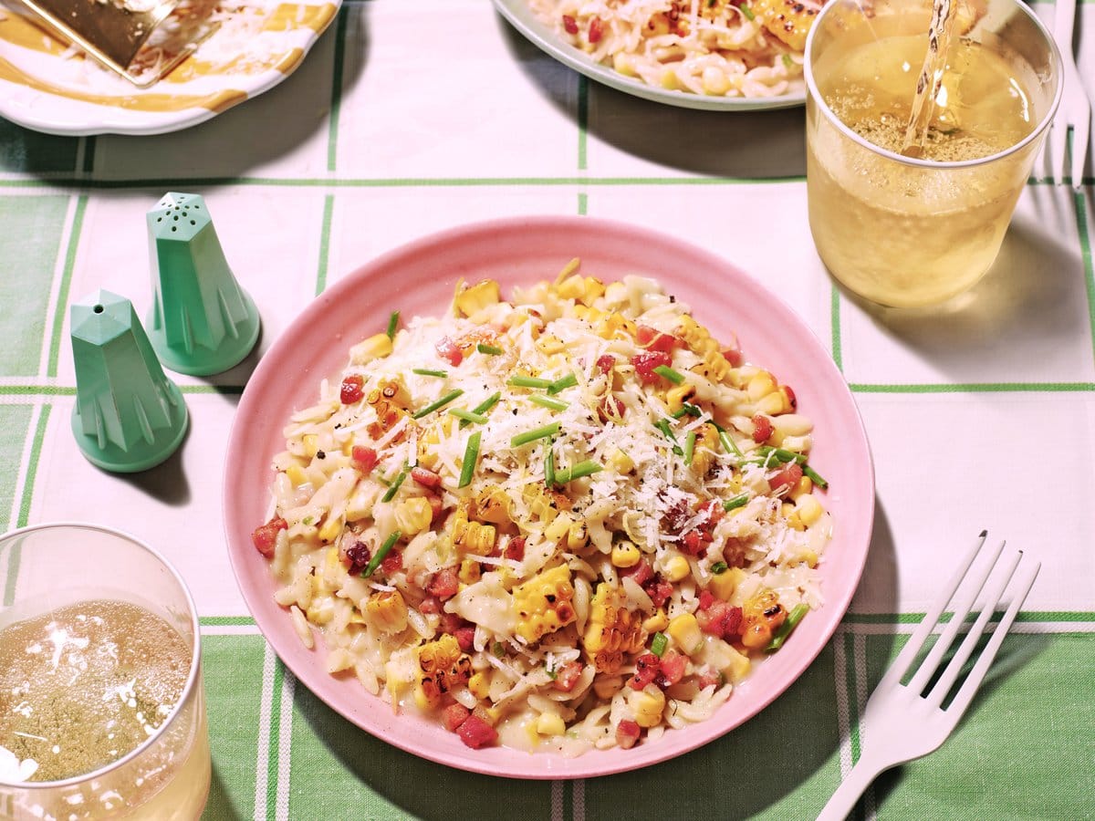 Gedekte tafel meet twee borden met orzotto met maïs, pancetta, parmezaanse kaas en bieslook