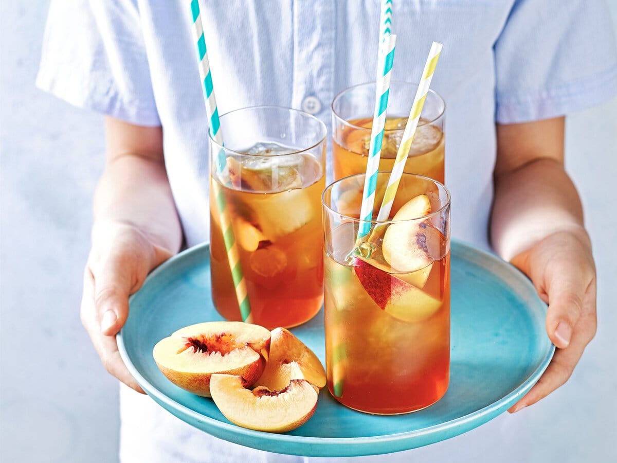 Drie glazen perzikijsthee met perziken ernaast