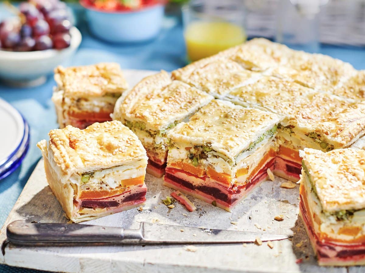 Taart van bladerdeeg met regenbooglaagjes van groenten in vierkante stukjes