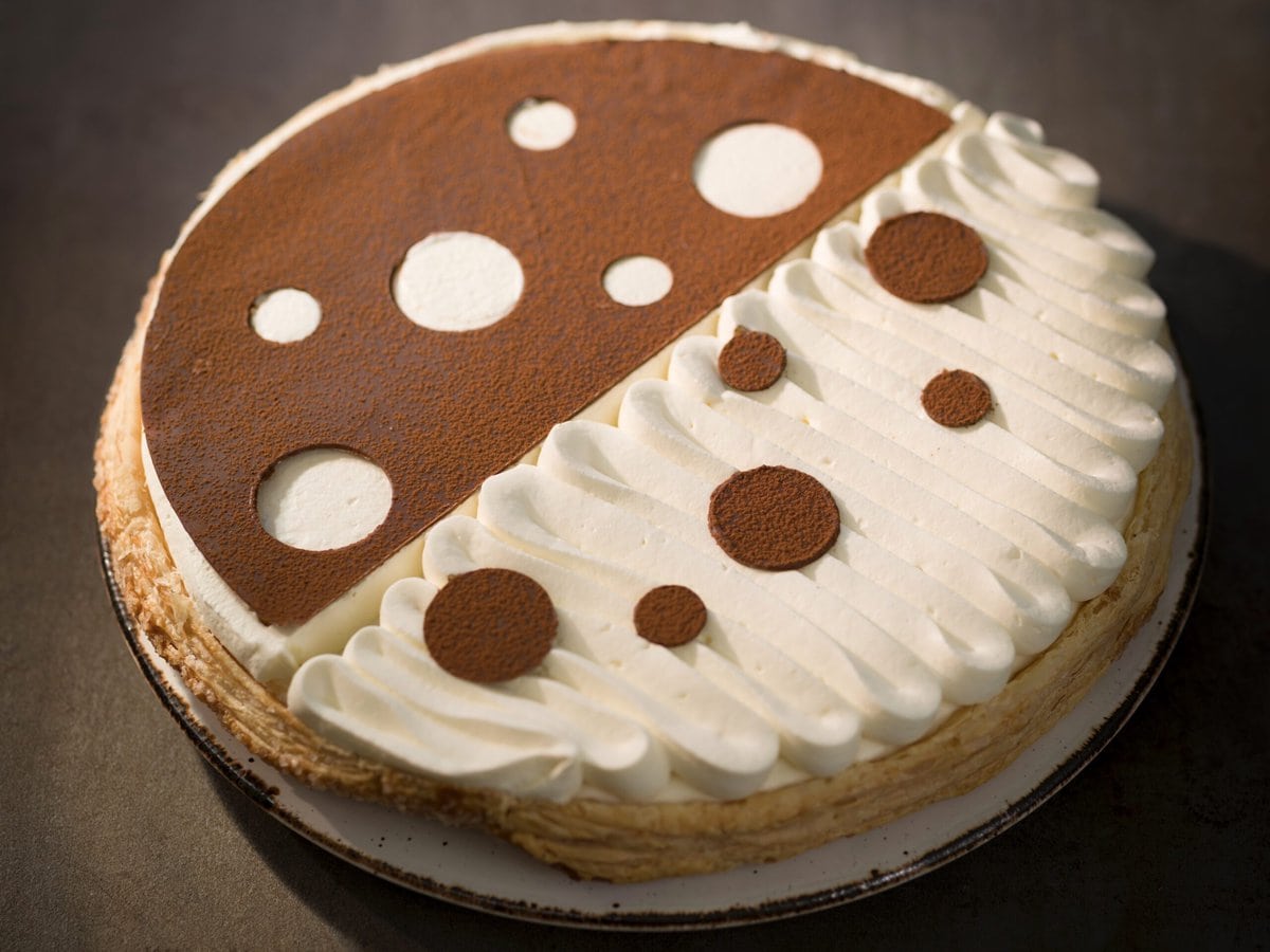 Stracciatella taart met rijstbavarois op bladerdeegbodem en daarop een halve plak chocolade en bolletjes chocolade