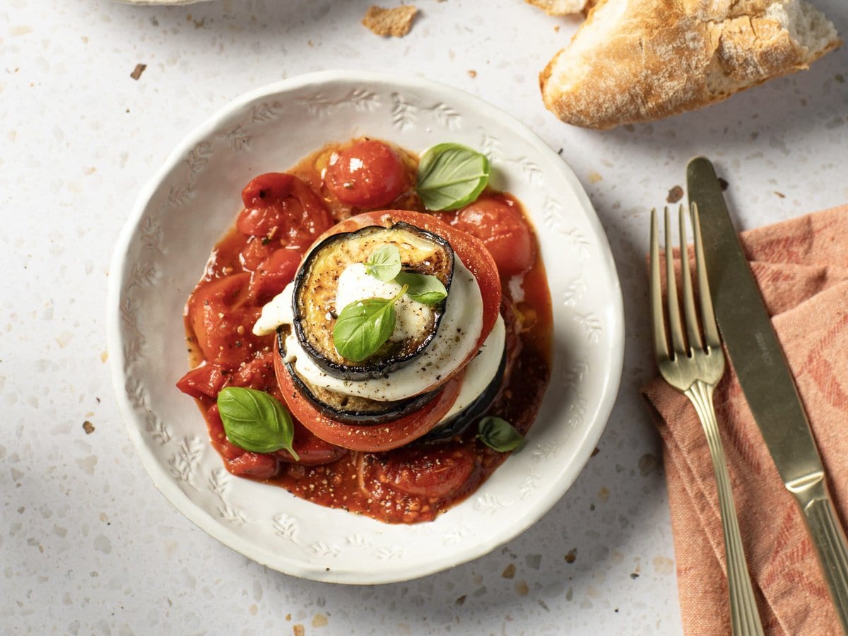 Torentje van aubergine en buffelmozzarella op een bedje van tomaat