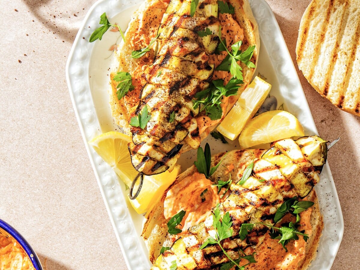 Twee spiesjes met aubergine en kip op platbrood met peterselie en citroen erbij