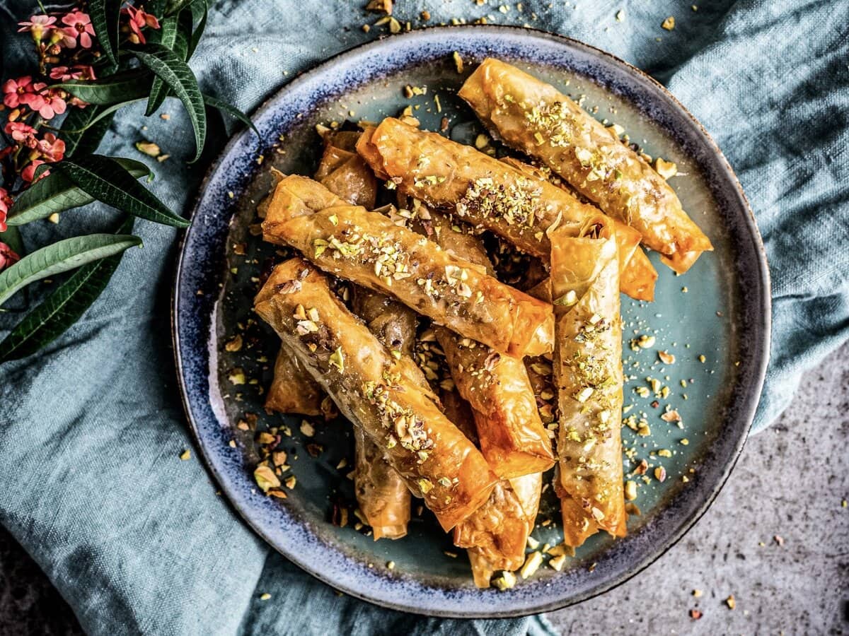 Langwerpige baklavarolletjes met verkruimelde pistachenootjes erover