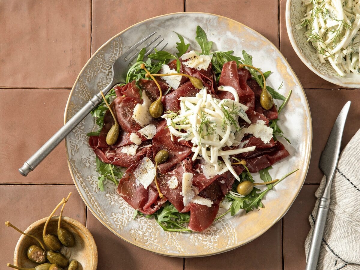 Bresaola-carpaccio op een bedje van rucola met Parmiggiano Reggiano, kapperappeltjes en knolselderij-appelsalade