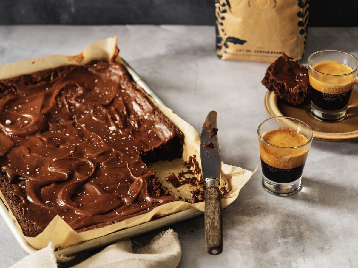 Espressobrownie met een mokkaglazuur laag en een stukje eruit, met twee espresso's ernaast