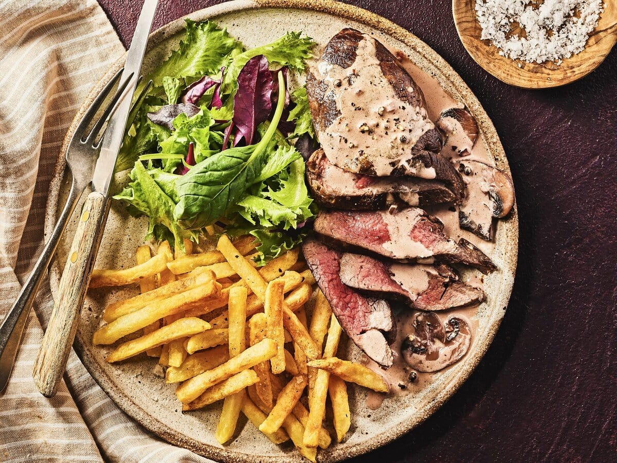 Bord met hertenbiefstuk met kastanjechampignon-pepersaus, friet en een groene salade