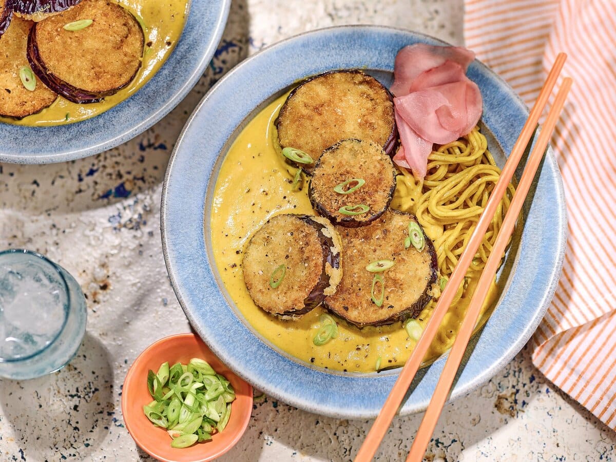 Gefrituurde aubergine met noedels en een kerrie saus met daarover lente-uitjes