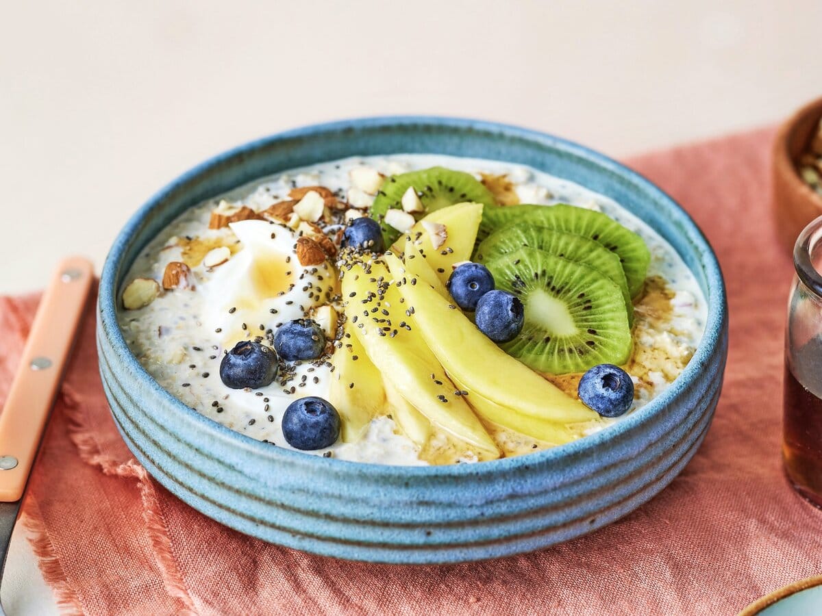 Ontbijtbowl van havermout met mango, kiwi, blauwe bes, ahornsiroop, chiazaad en noten