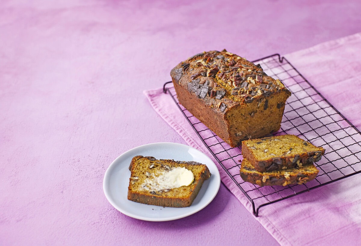 Pompoenbrood met chocolade en pecannoten op een rooster met daarnaast een sneetje met boter