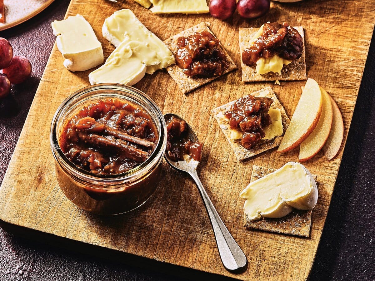 Kaasplankje met kaas, toastjes en een pot vijgenchutney die is gesmeerd op een paar toastjes