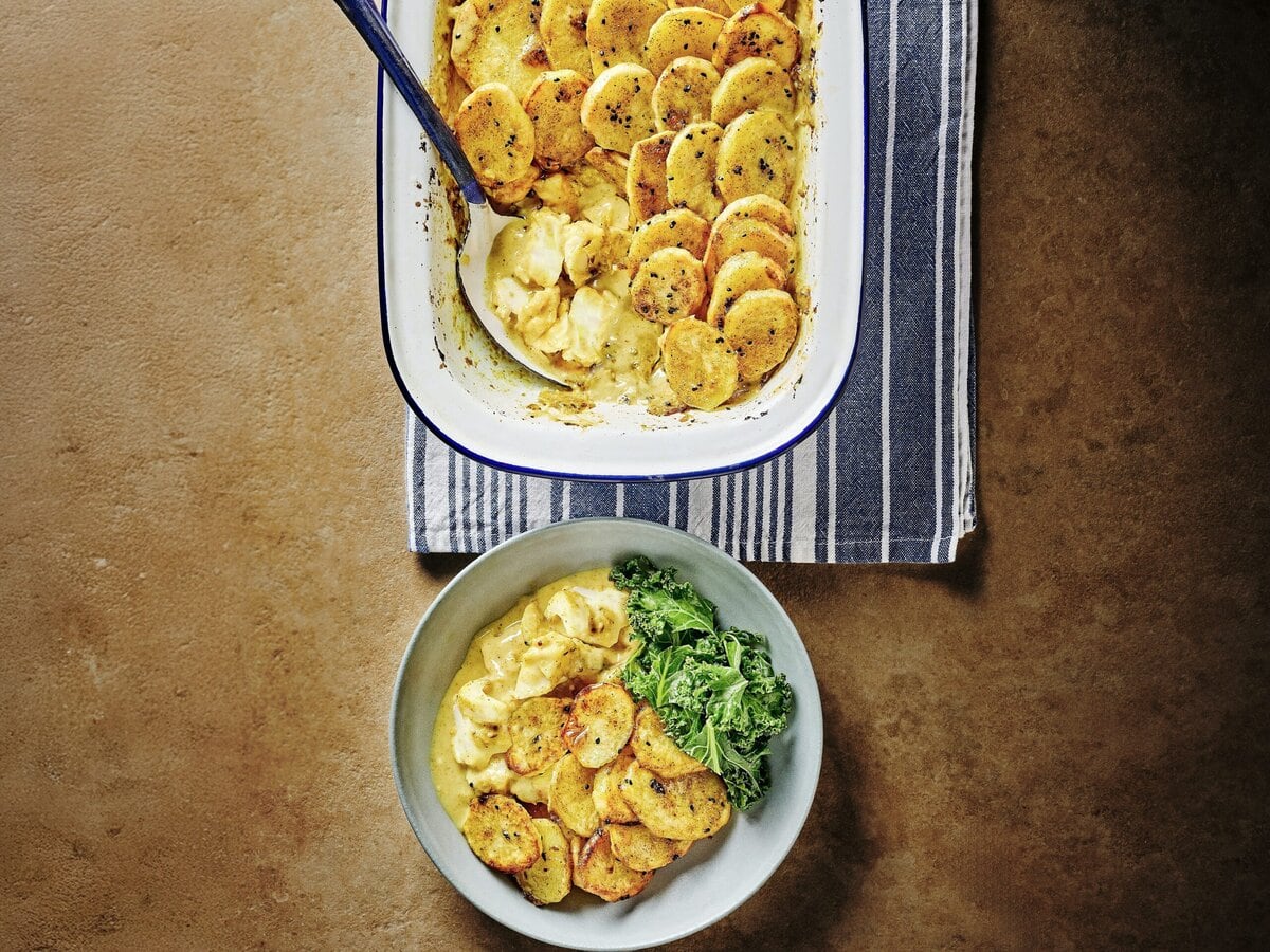Ovenschaal en bord met viscurrypie met krokante aardappel erop en daarnaast gekookte groene groente