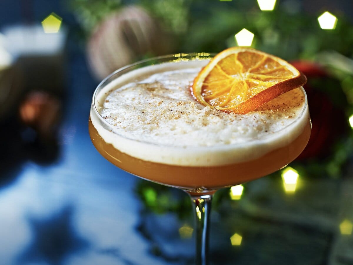 Oranje cocktail met schuimaalgje in cocktailglas met snufje nootmuskaat en gedroogd plakje sinaasappel