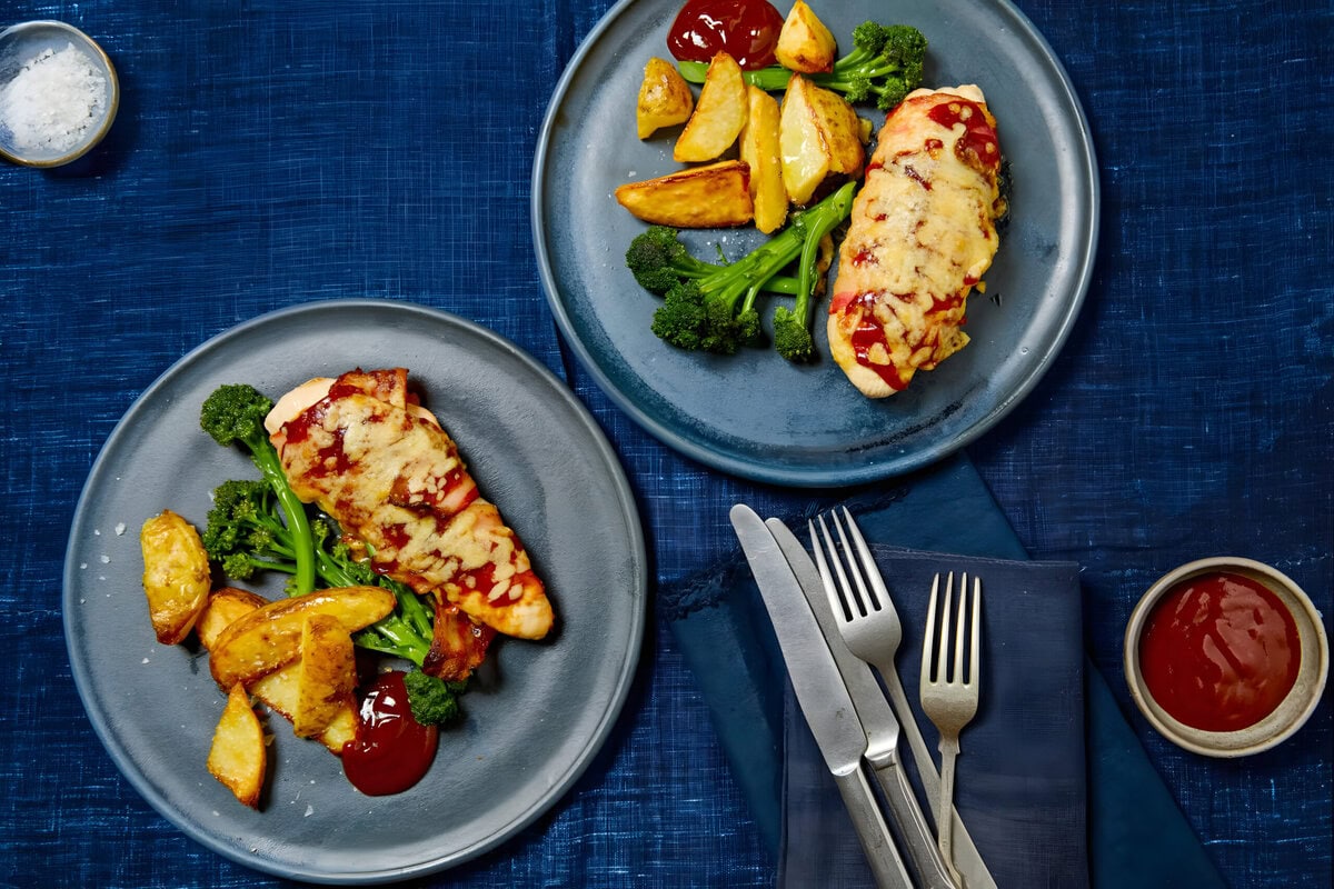 Twee borden barbecuekip met bacon en cheddar, met daarnaast aardappelpartjes en aspergebroccoli