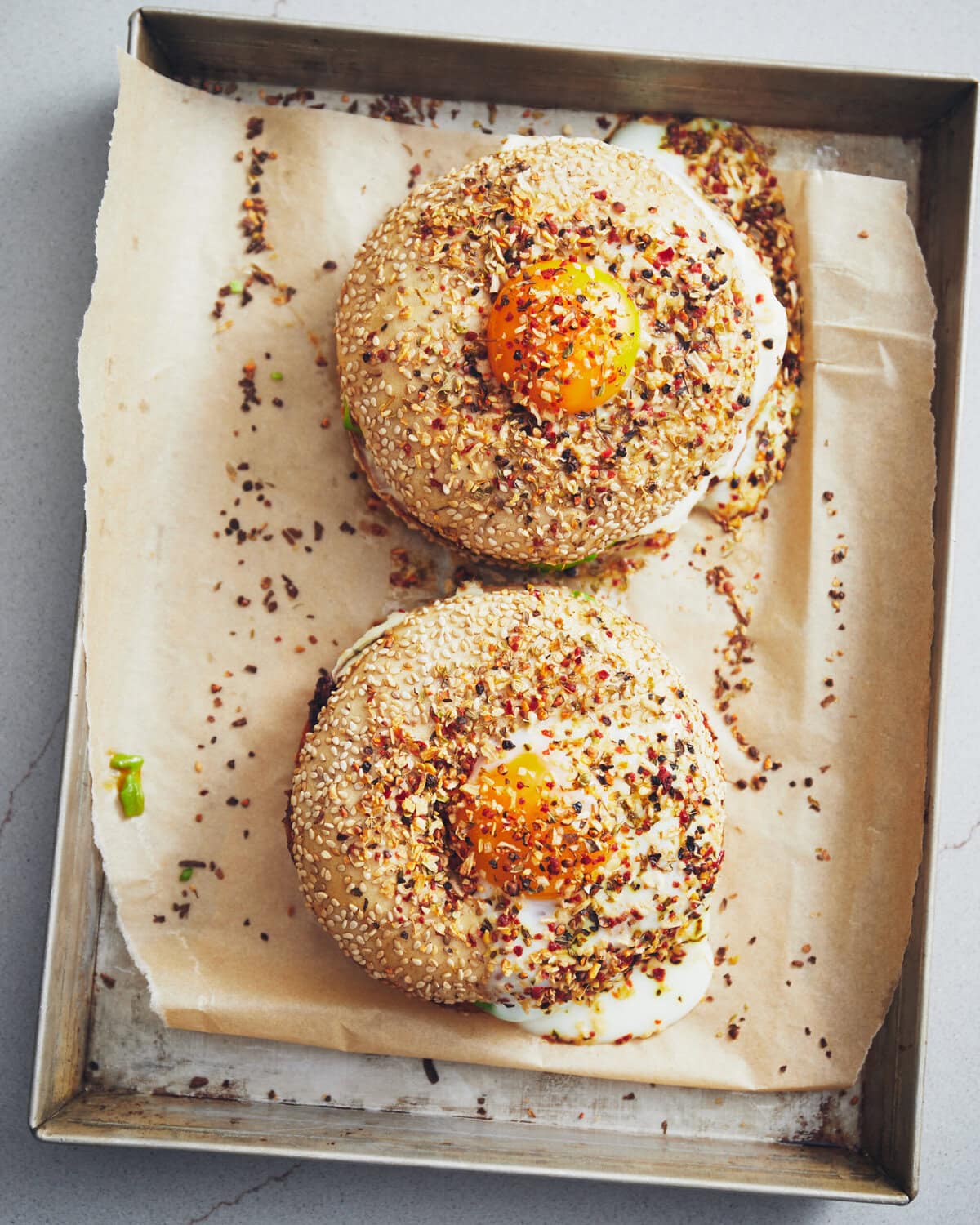 Twee bagels met sesamzaad, met in het midden eigeel en daarover chilivlokken