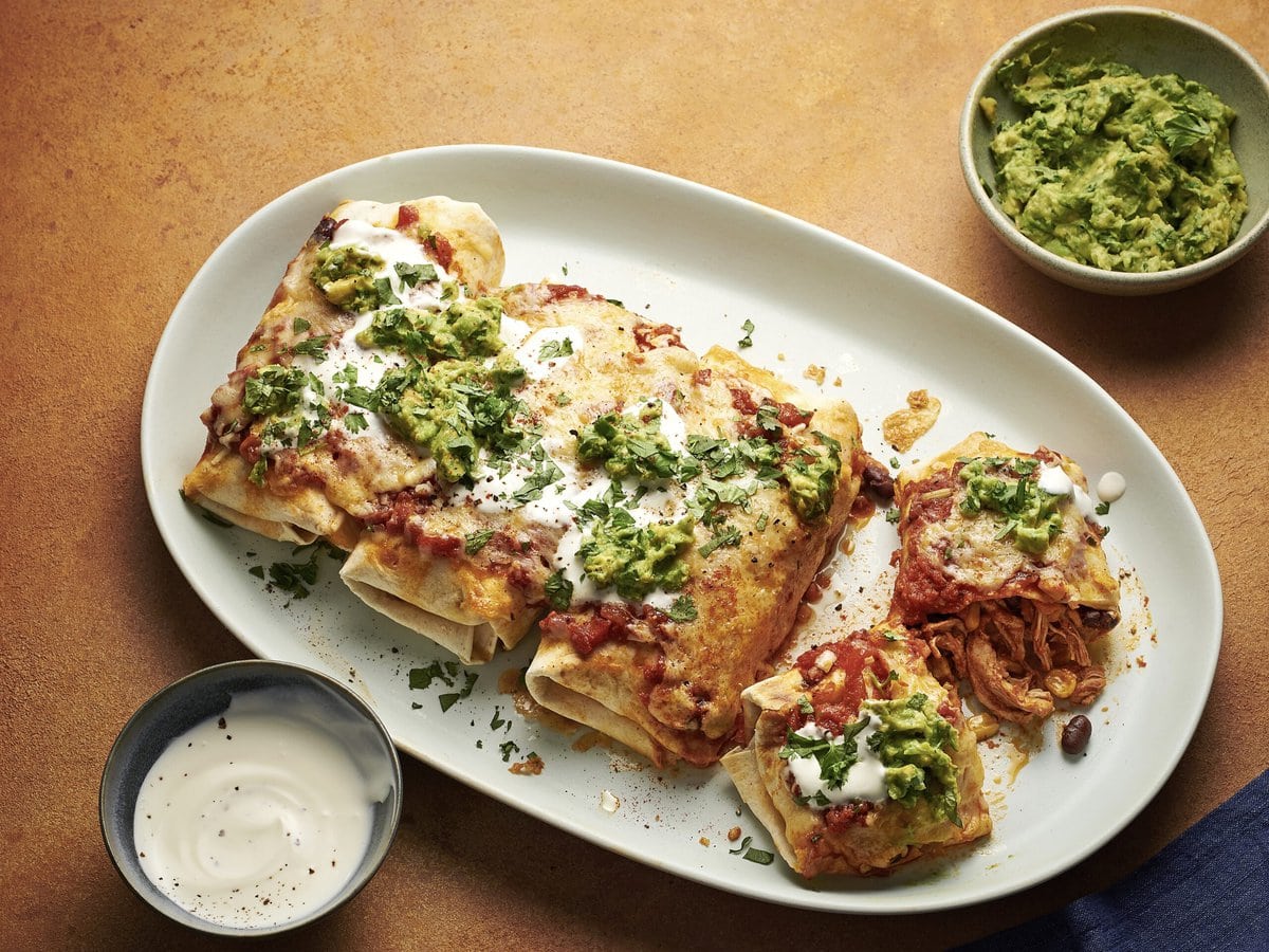 Vier enchilada’s met kip en bonen uit de slowcooker, bestrooid met kaas, zure room en guacamole