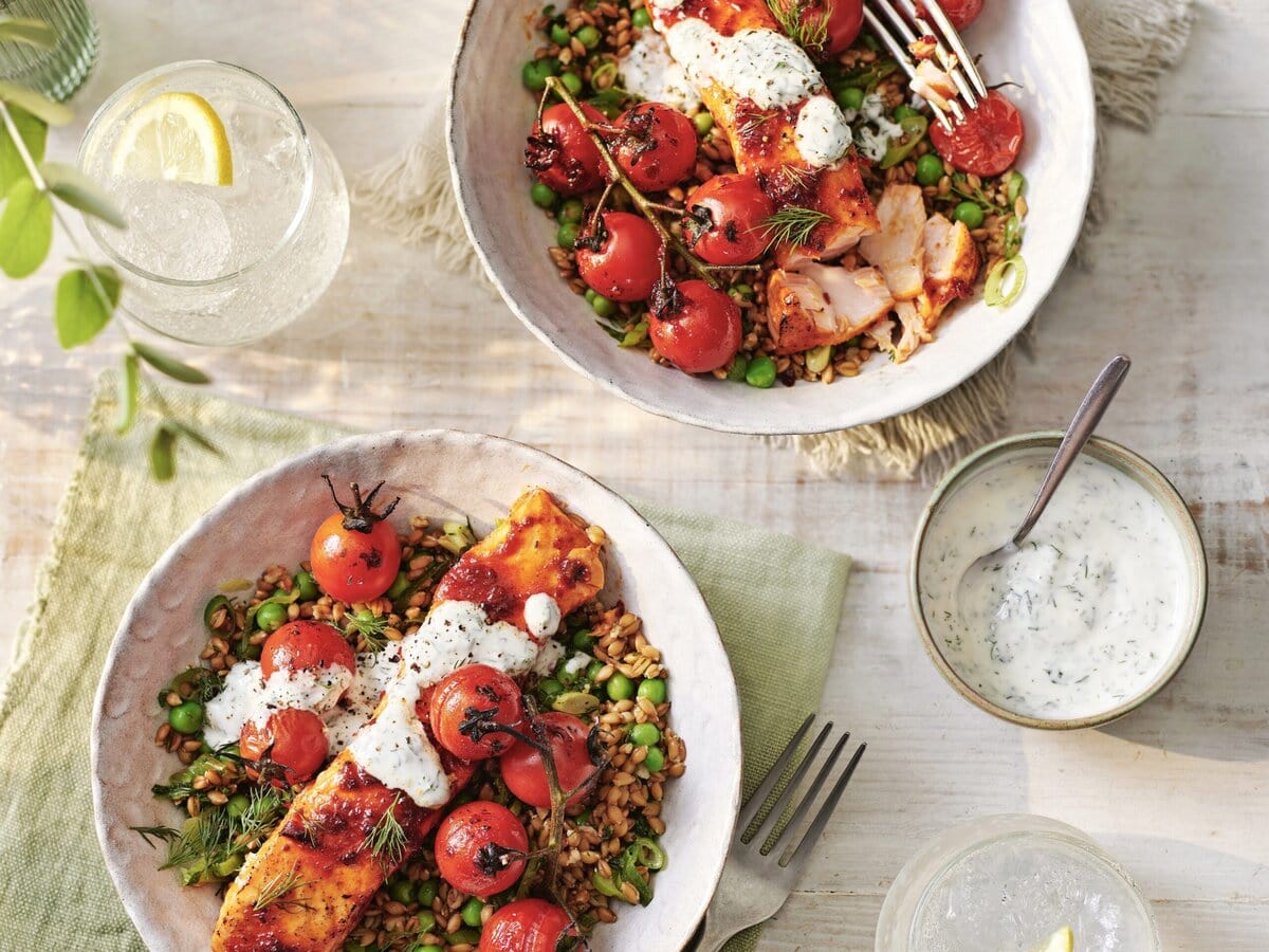 2 bakjes gebakken zalm met harissa, kruidige parelspelt, erwten, cherrytomaten en yoghurtdressing