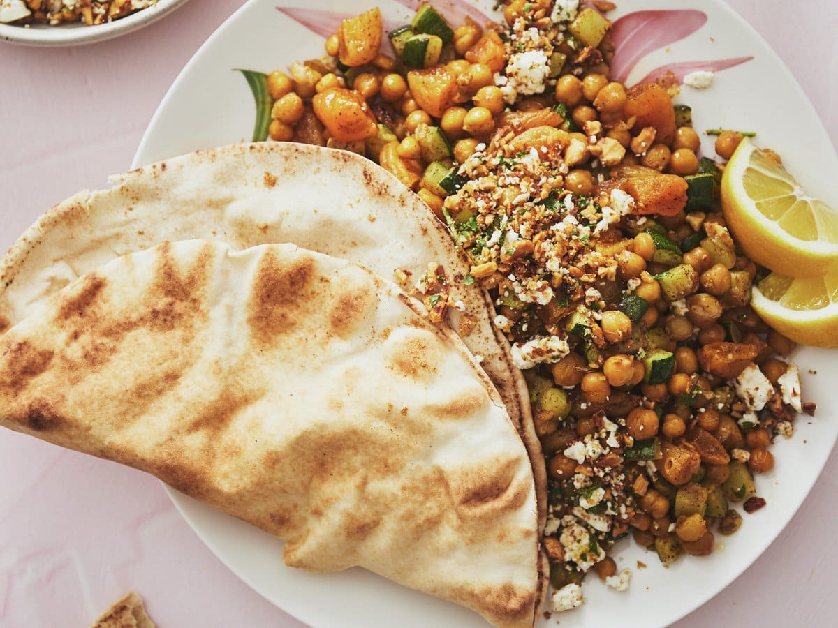 Kikkererwten met abrikoos, courgette, feta, amandelen en peterselie, geserveerd met partjes citroen en Libanees platbrood