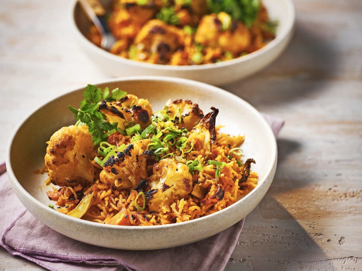 Twee borden Koreaanse rijsttraybake met bloemkool en wortel, afgetopt met lente-ui en koriander