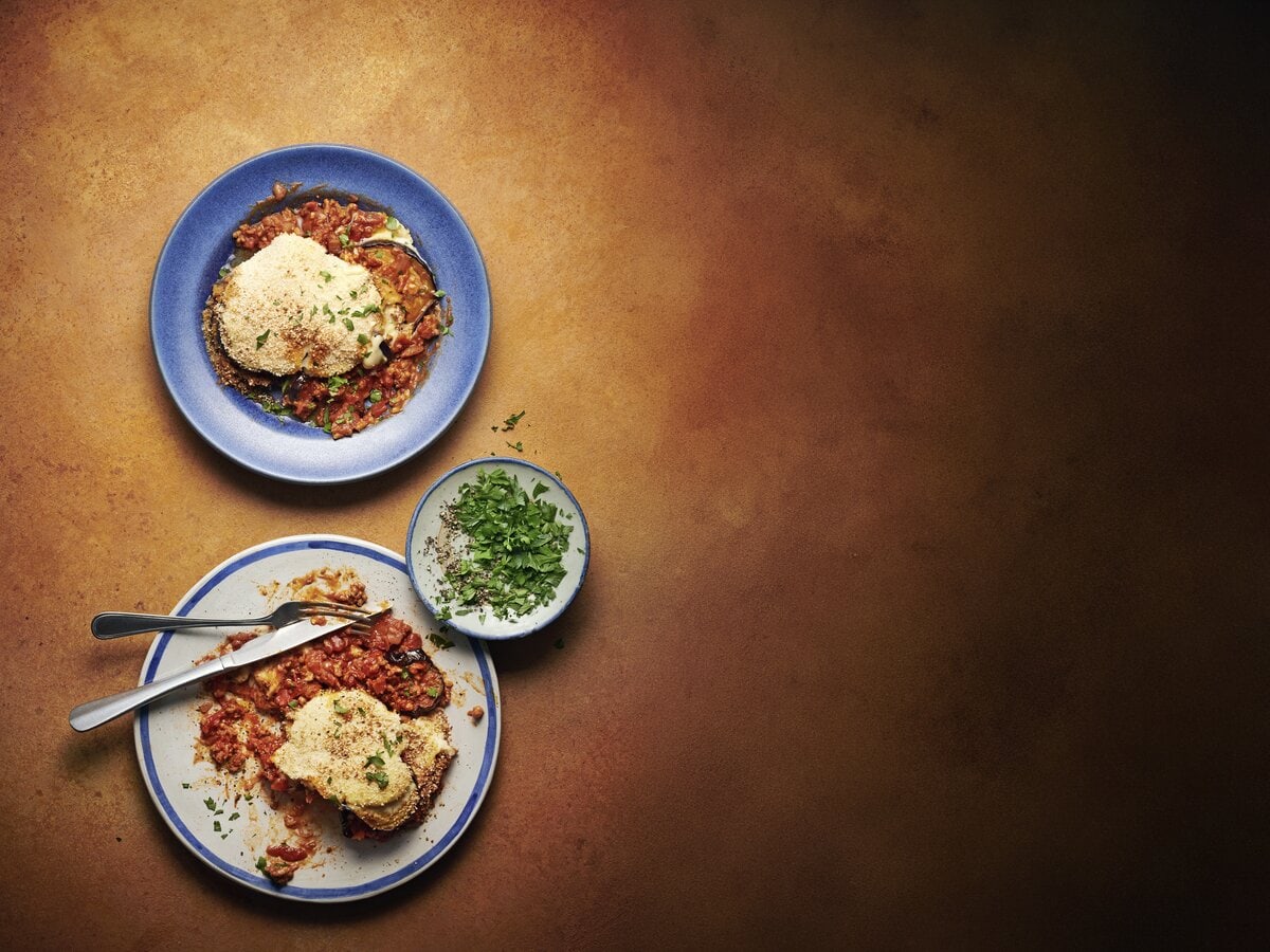 Twee borden moussaka met bovenop bechamelsaus en paneer, geserveerd met peterselie