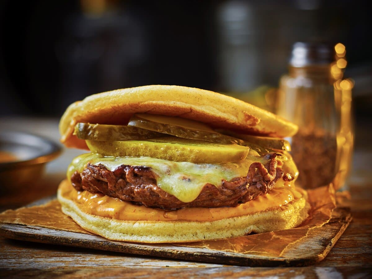 Twee pannenkoeken als broodjes, met daartussen een smashburger, kaas, augurk en burgersaus