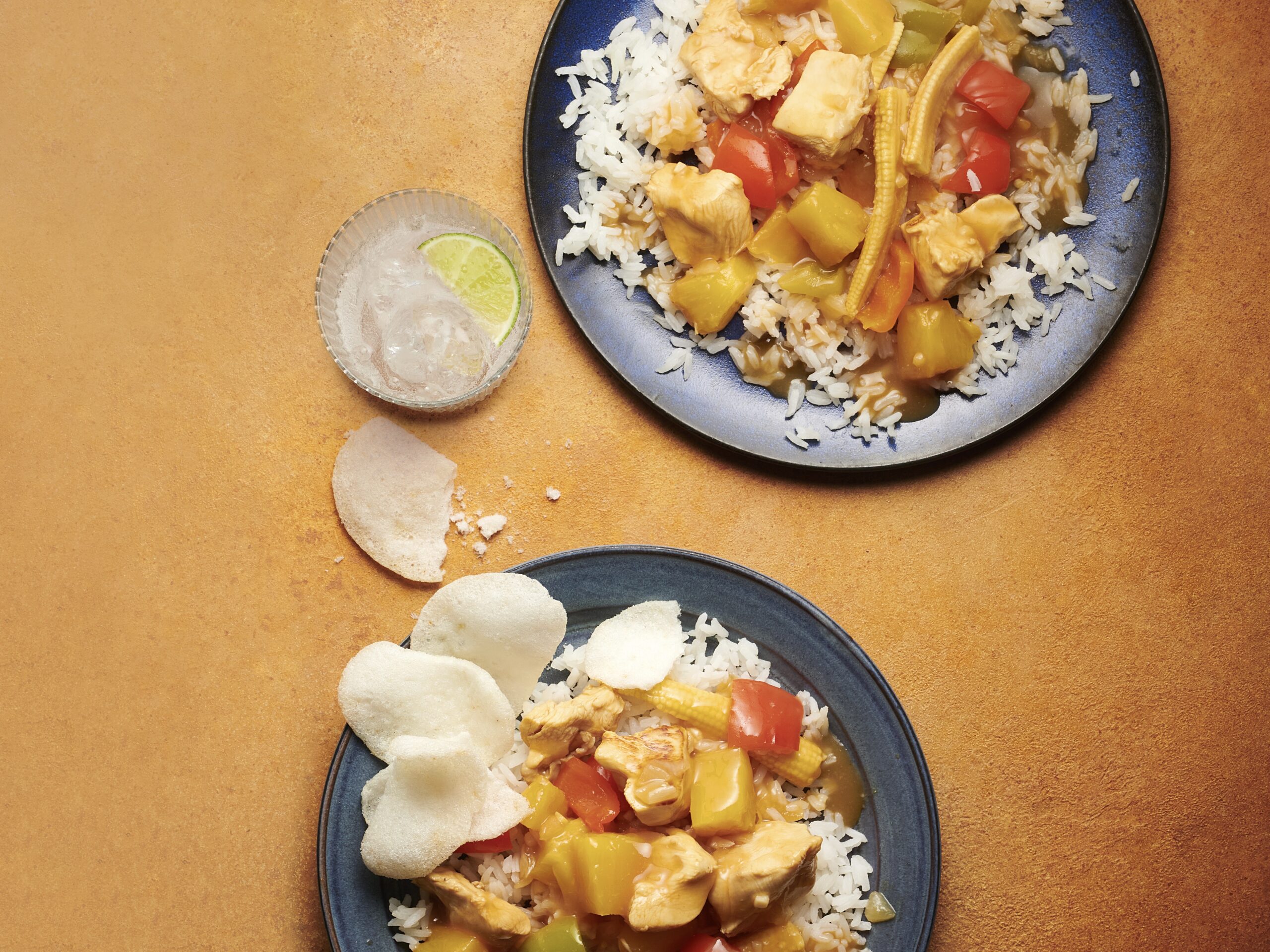 Twee borden zoetzure kip met ananas, babymaïs en paprika, geserveerd met witte rijst en kroepoek