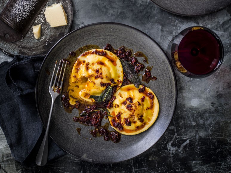 ravioli-met-eidooier-en-nduja op een bord met een glas wijn
