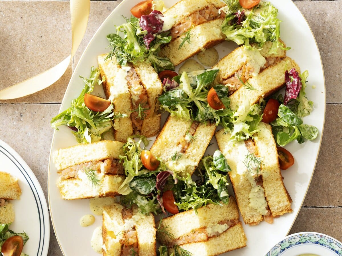 Stukjes briochetoast met tartaar van gerookte zalm en citroendressing, geserveerd tussen gemengde salade met tomaatjes