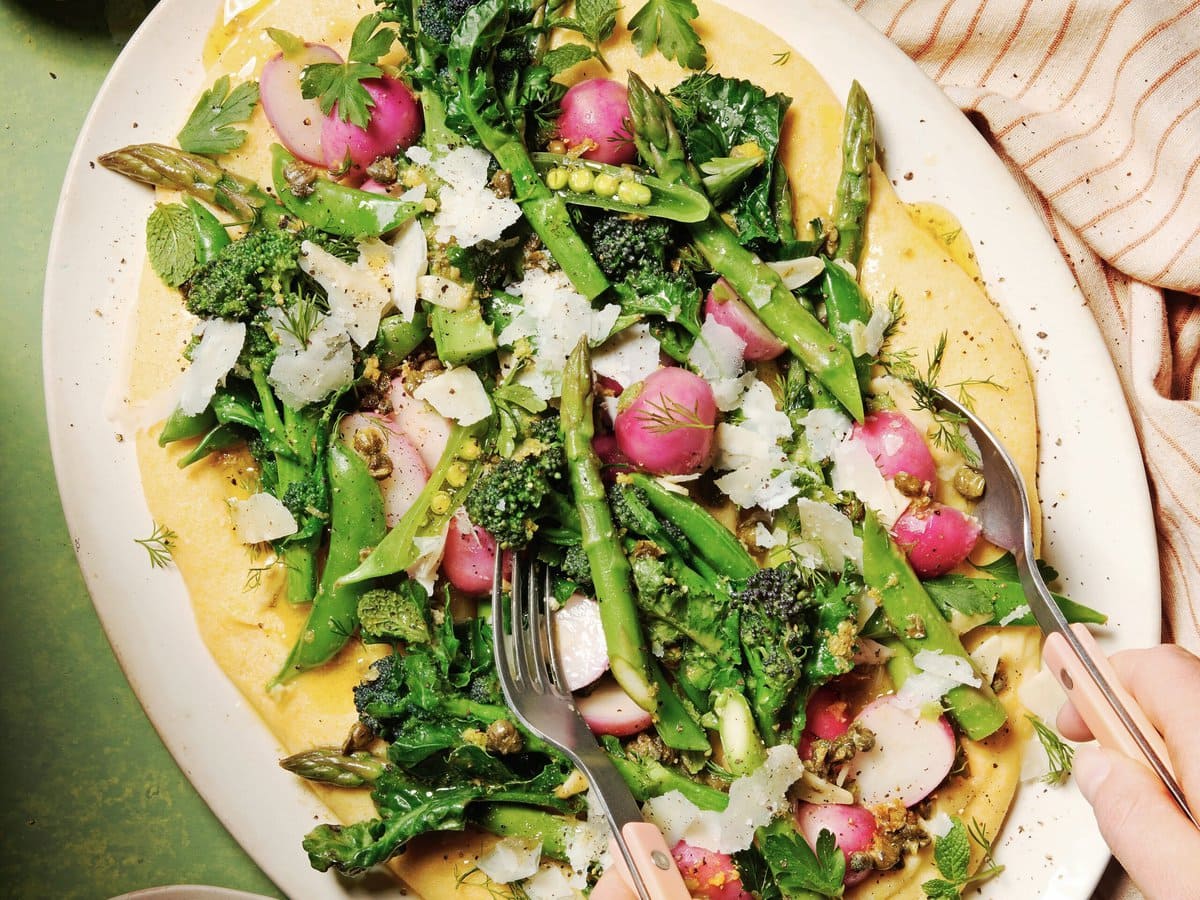Schaal met kaaspolenta en daarop een salade van aspergebroccoli, radijs, sugarsnaps en groene asperges met Parmezaanse kaas erover