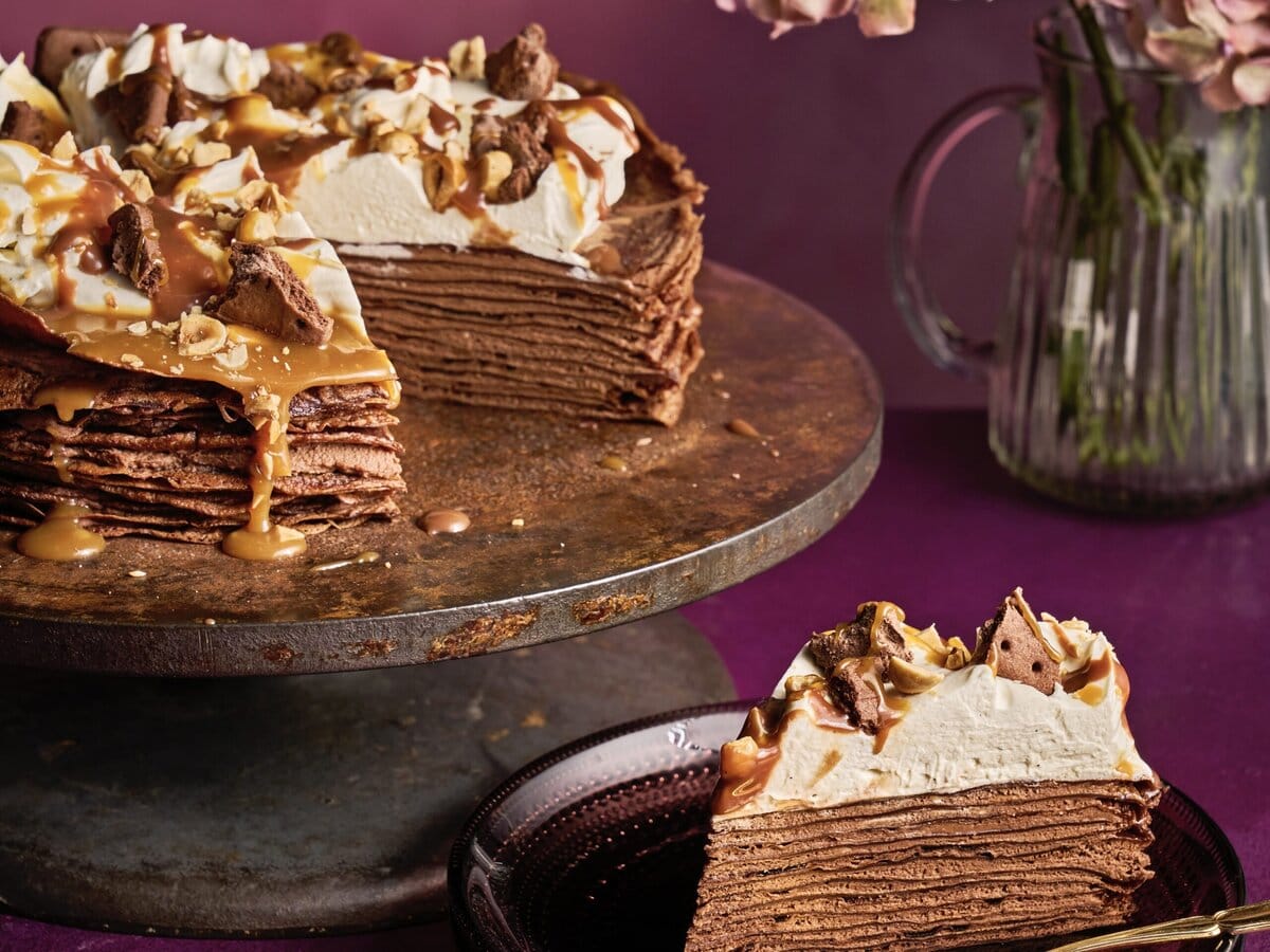 Mississippi-mud-pie-pannenkoeken-taart met laagjes pannenkoek, chocoladecustard en bovenop crème en caramelsaus met een stukje eruit gesneden