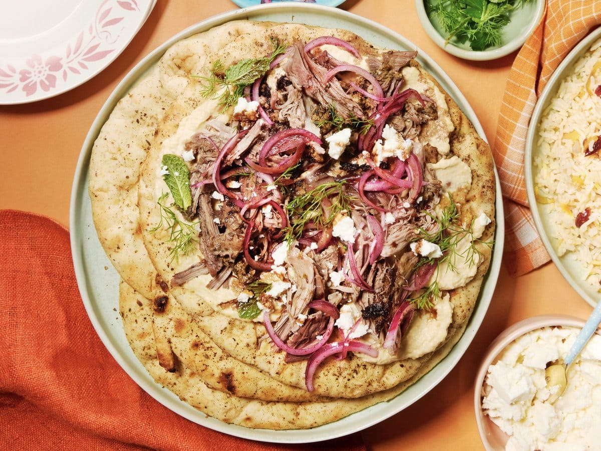 Platbrood met uit elkaar gevallen lamsvlees met een feta-walnootkorst en granaatappelmelasse, rode ui en hummus
