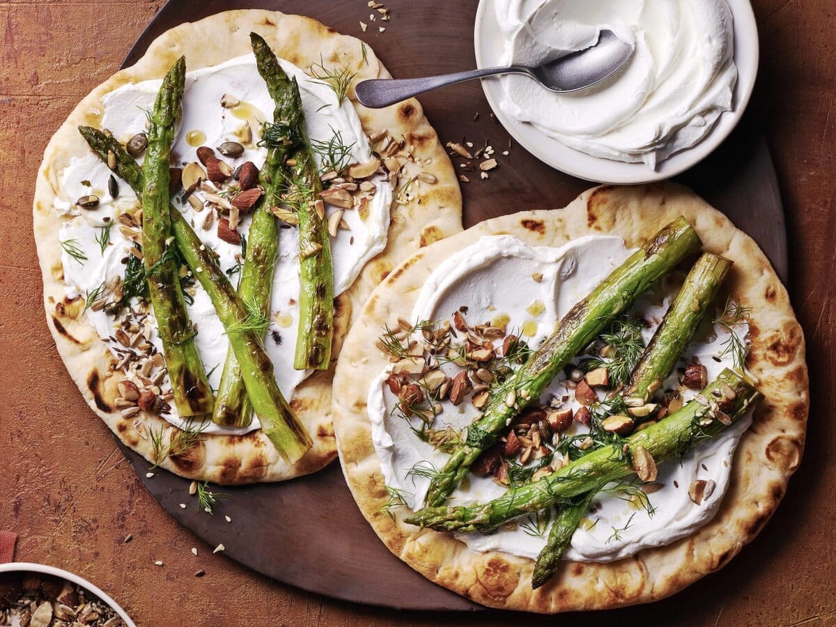 Twee platbroden met labneh en daarop geroosterde groene asperges en dukkah