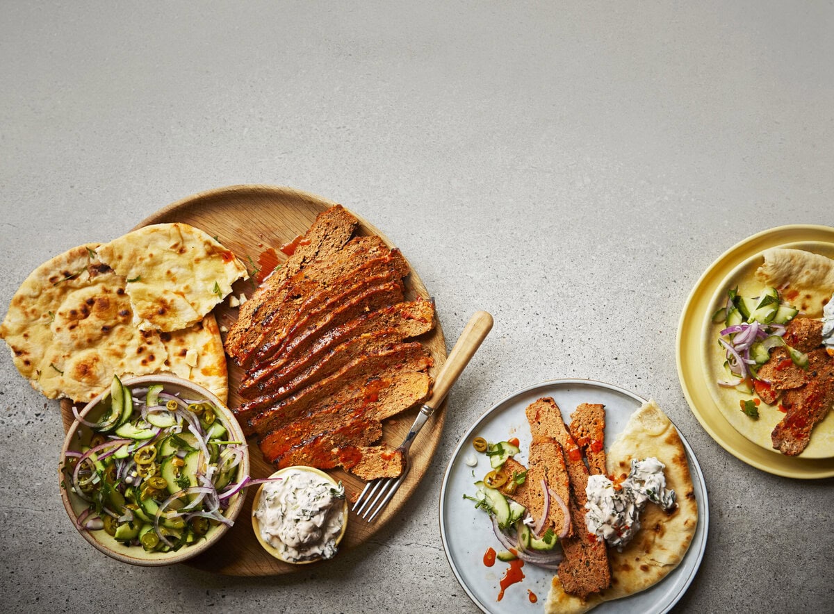 Bord met lamskebab, platbrood, saus en een salade van komkommer, rode ui en olijven