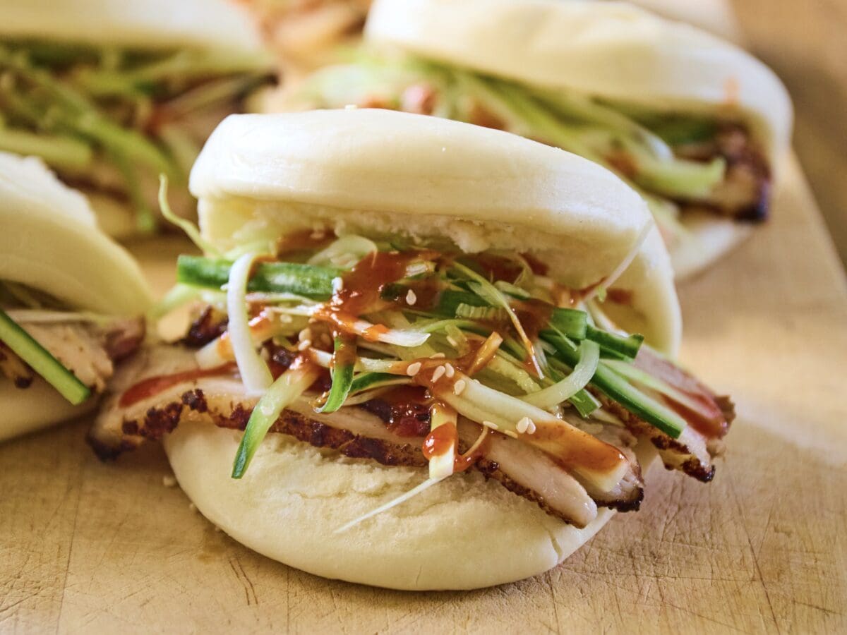 Bao buns met Chinees gemarineerd buikspek, met daarop reepjes komkommer, marinade en sesamzaadjes