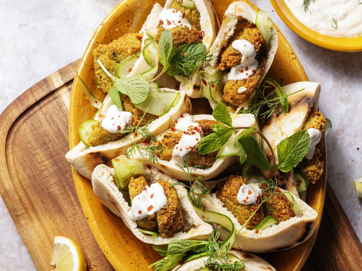 Halve pita broodjes, gevuld met gebakken falafel, komkommerlinten, knoflooksaus en bestrooid met chilivlokken en takjes munt
