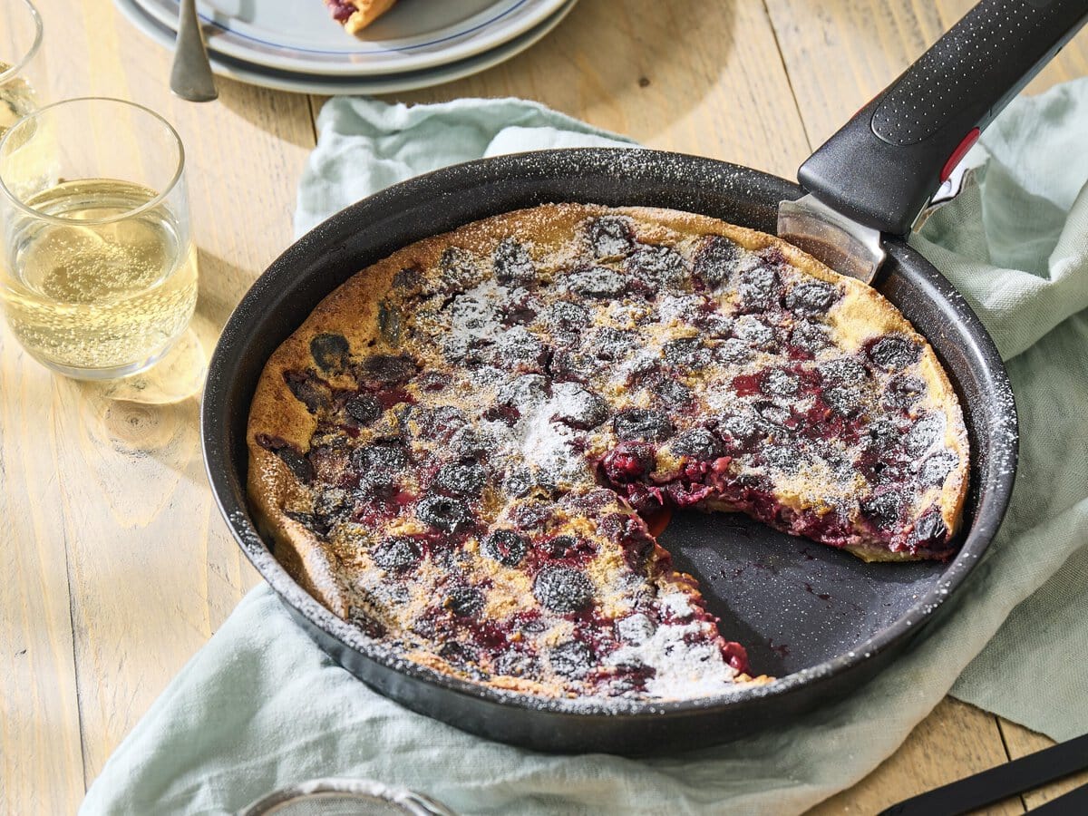 Clafoutis met kersen en sinaasappelrasp in een pan, bestrooid met poedersuiker