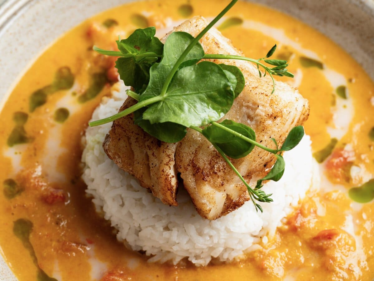 Bolletje rijst met daarop kabeljauwfilet en waterkers, met om de rijst een rode curry