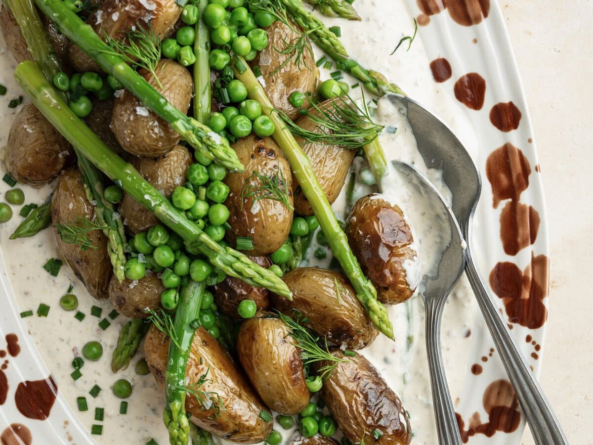 Salade met onderop dressing en daarop krieltjes, doperwtjes, groene asperges, dille en bieslook