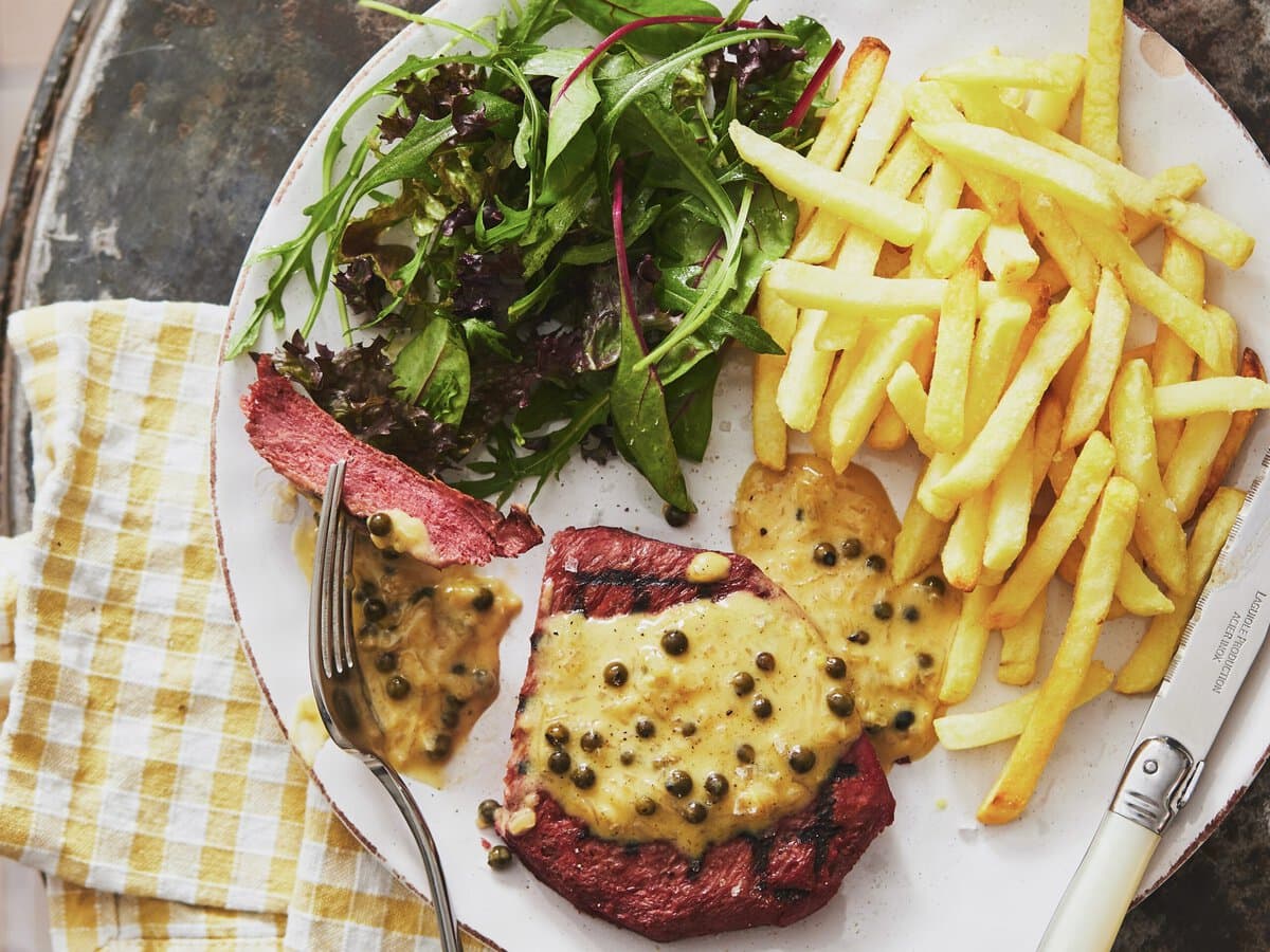 Gegrilde vega steak met pepersaus, geserveerd met dunne frietjes en een groene salade