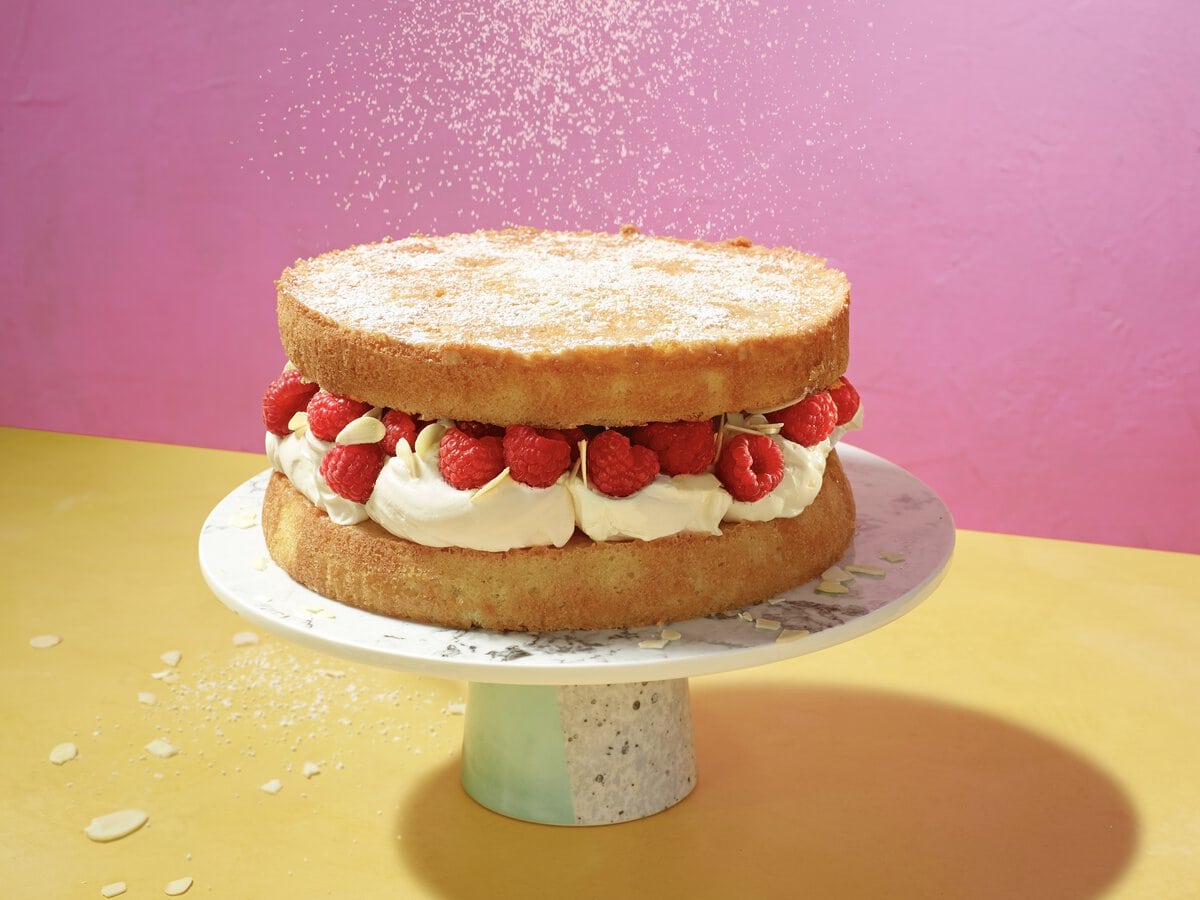 Twee luchtige cakes met daartussen een witte crème, frambozen en amandelschaafsel