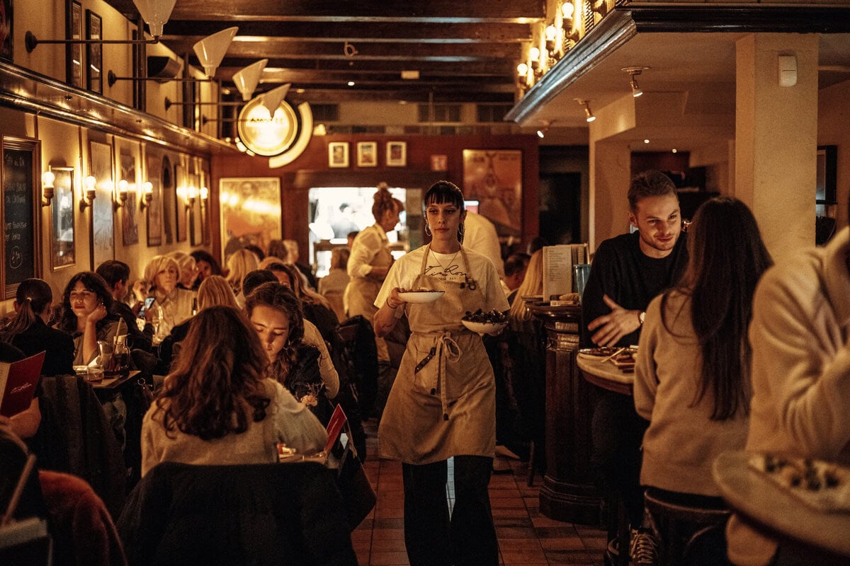 Druk, donker café waar een serveerster met twee borden loopt
