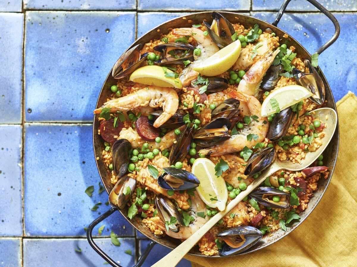 Paella mixta met mosselen, garnaal, kip, doperwten, koriander en citroenpartjes