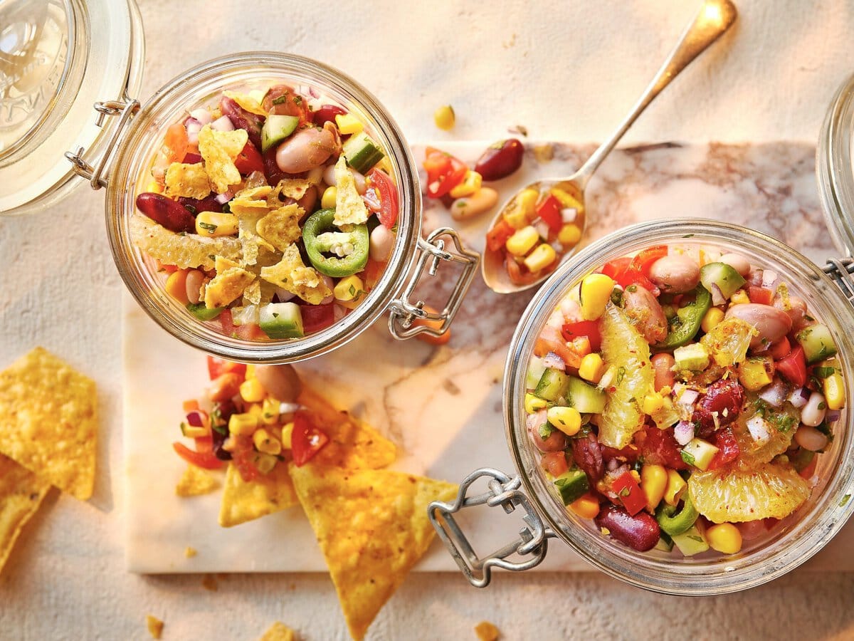 Twee potjes salade met onder andere bonen, rode ui, paprika en mais, geserveerd met tortillachips