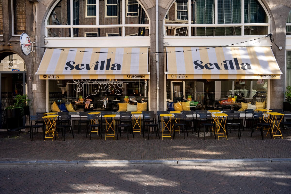Terras met wit-geel gestreepte luifel en geel en zwarte tafels