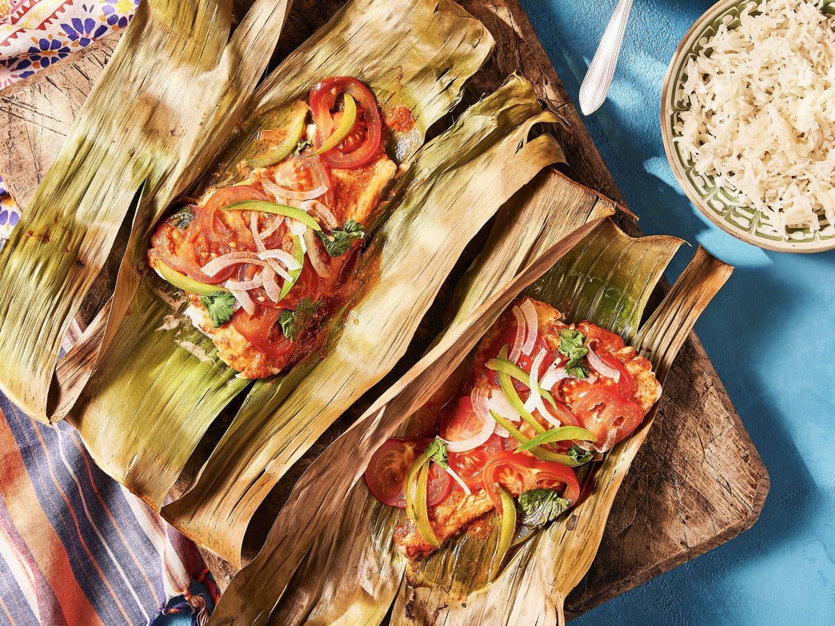 Vispakketjes met kruidenmarinade, groene paprika, tomaat en ui, geserveerd op een bananenblad