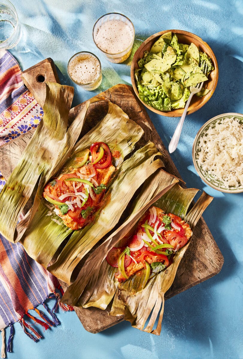 Vispakketjes met kruidenmarinade, groene paprika, tomaat en ui, geserveerd op een bananenblad